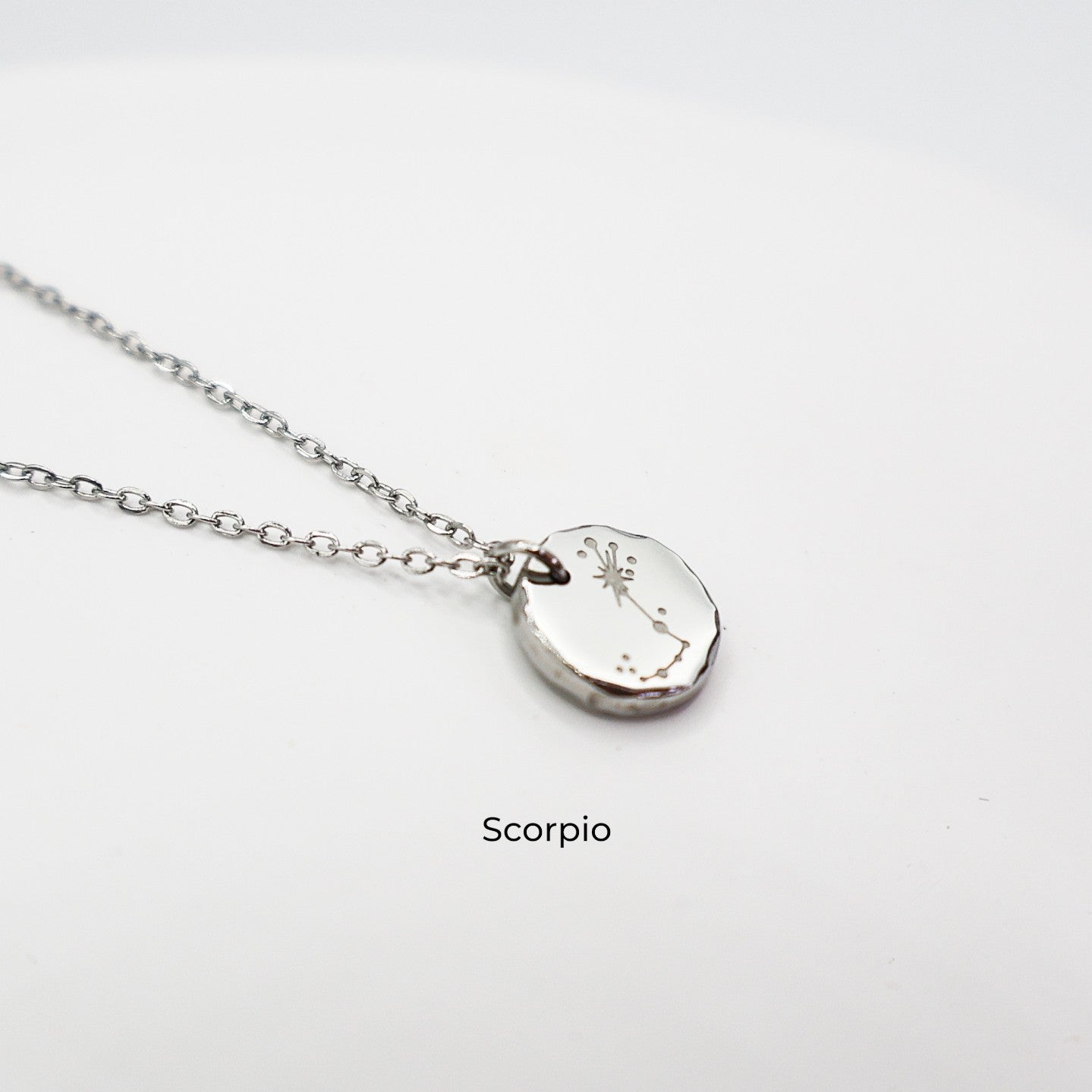 Silver necklace with a round pendant on a light gray background. The pendant is engraved with the Scorpio star sign constellation