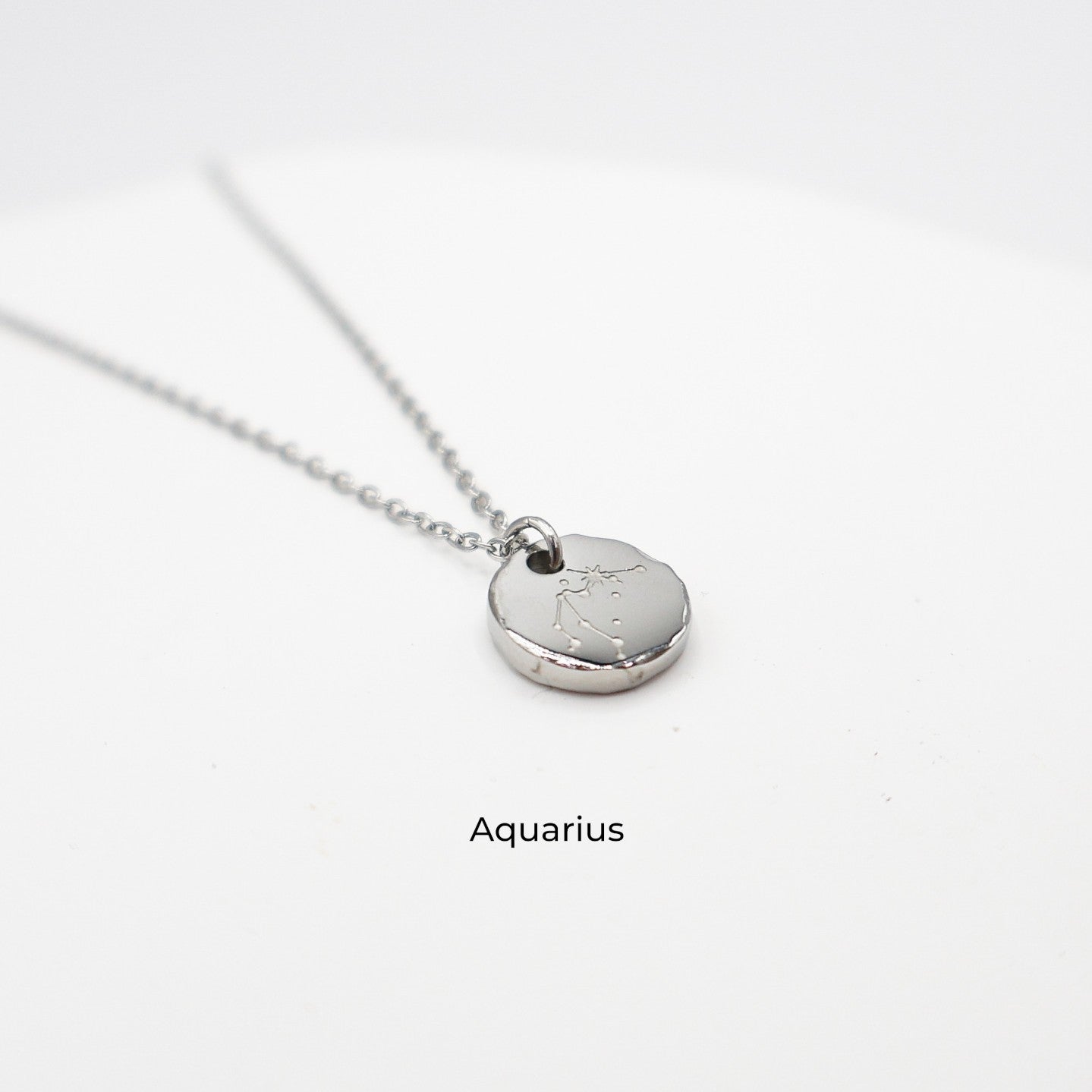 Silver necklace with a round pendant on a light gray background. The pendant is engraved with the Aquarius star sign constellation