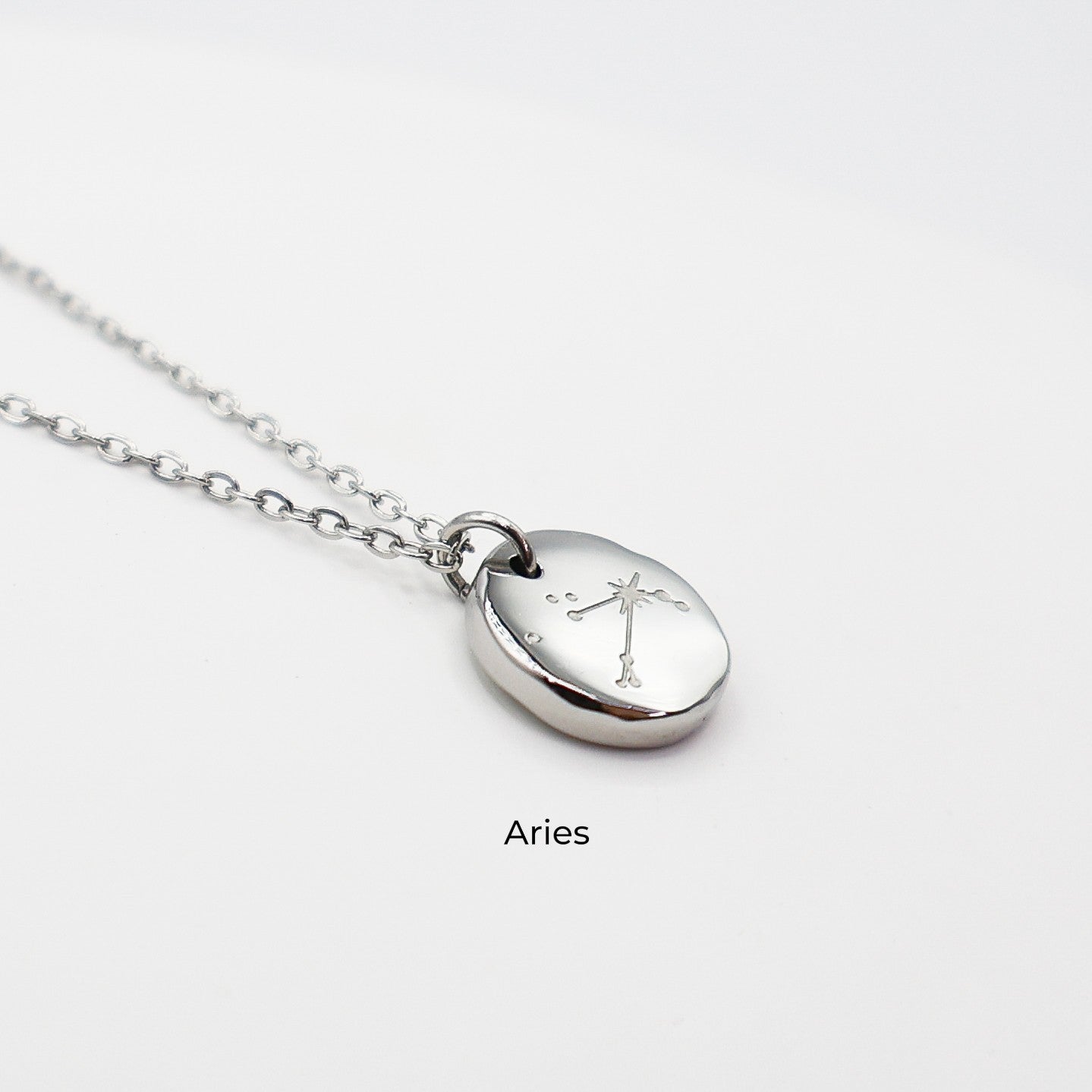 Silver necklace with a round pendant on a light gray background. The pendant is engraved with the Aries star sign constellation