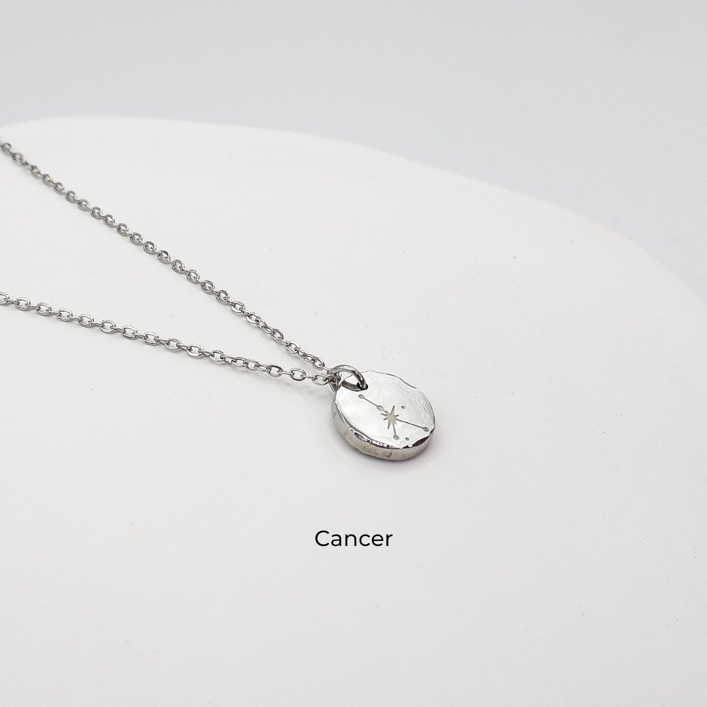 Silver necklace with a round pendant on a light gray background. The pendant is engraved with the Cancer star sign constellation