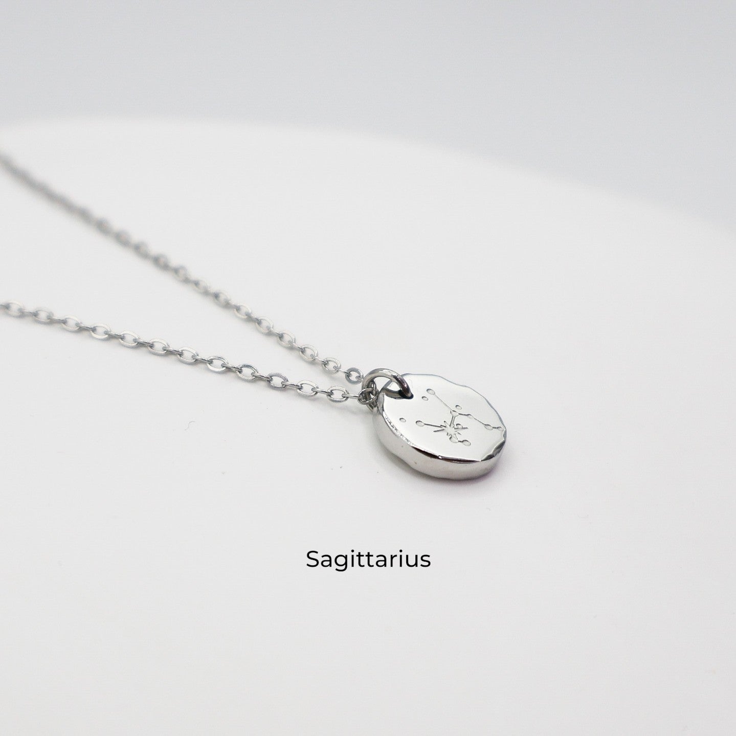 Silver necklace with a round pendant on a light gray background. The pendant is engraved with the Sagittarius star sign constellation