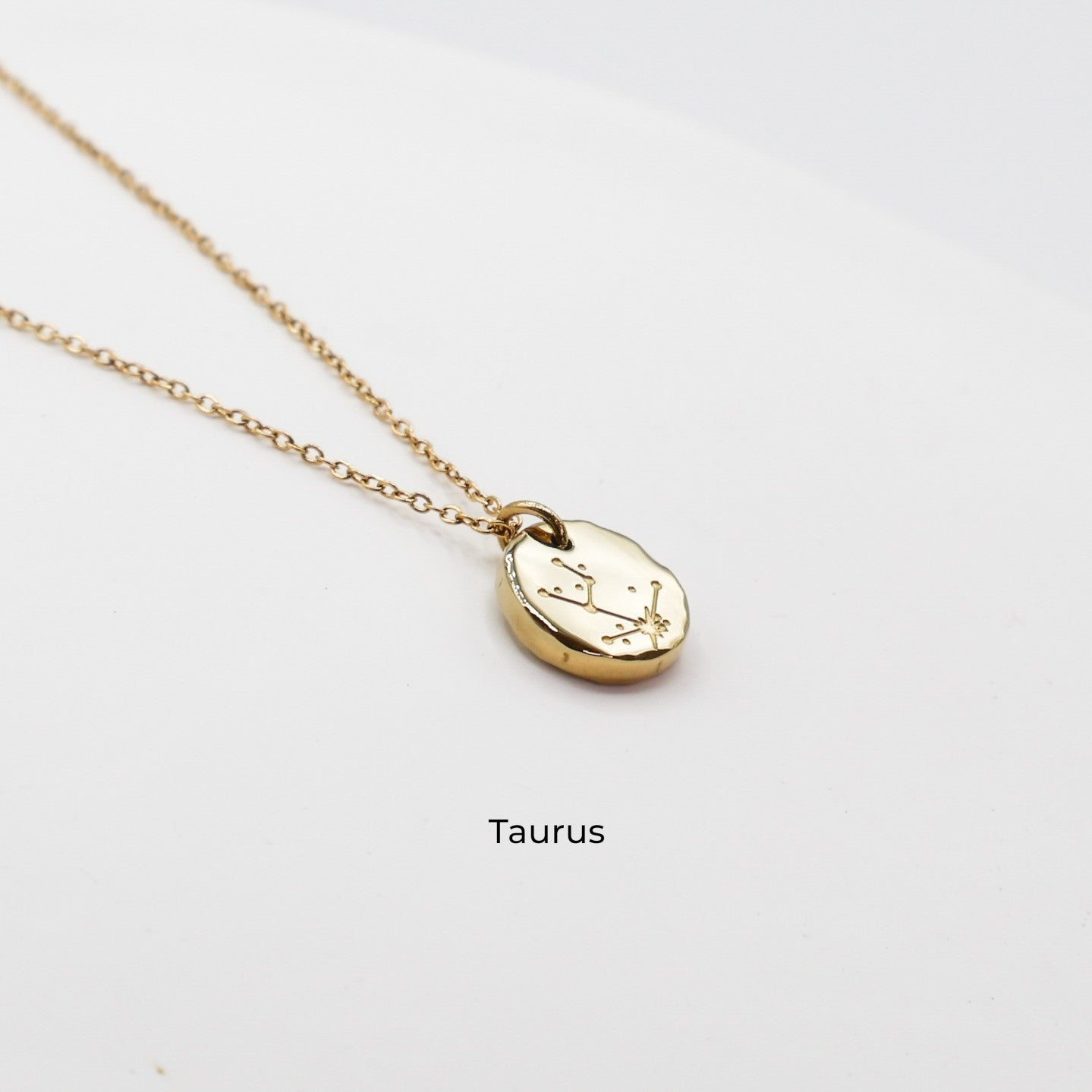 Gold necklace with a round pendant on a light gray background. The pendant is engraved with the Taurus star sign constellation
