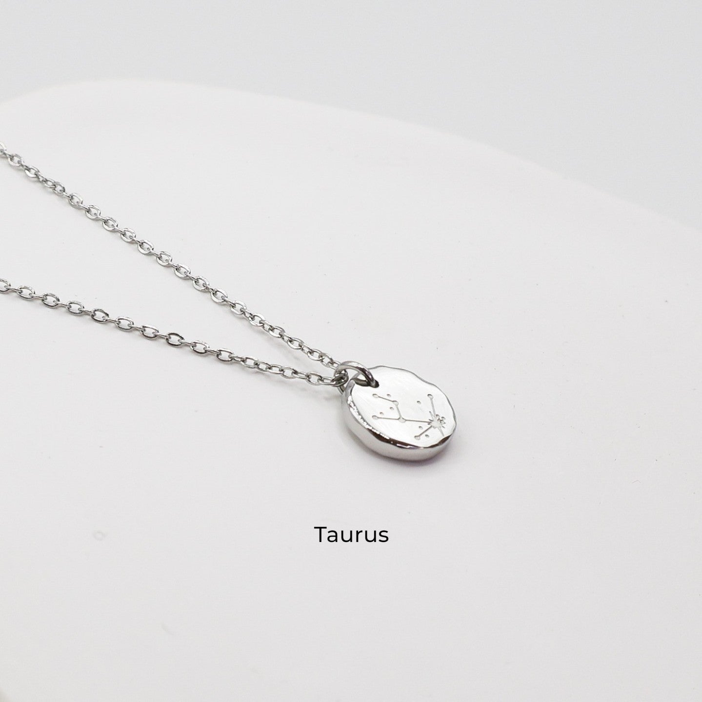 Silver necklace with a round pendant on a light gray background. The pendant is engraved with the Taurus star sign constellation