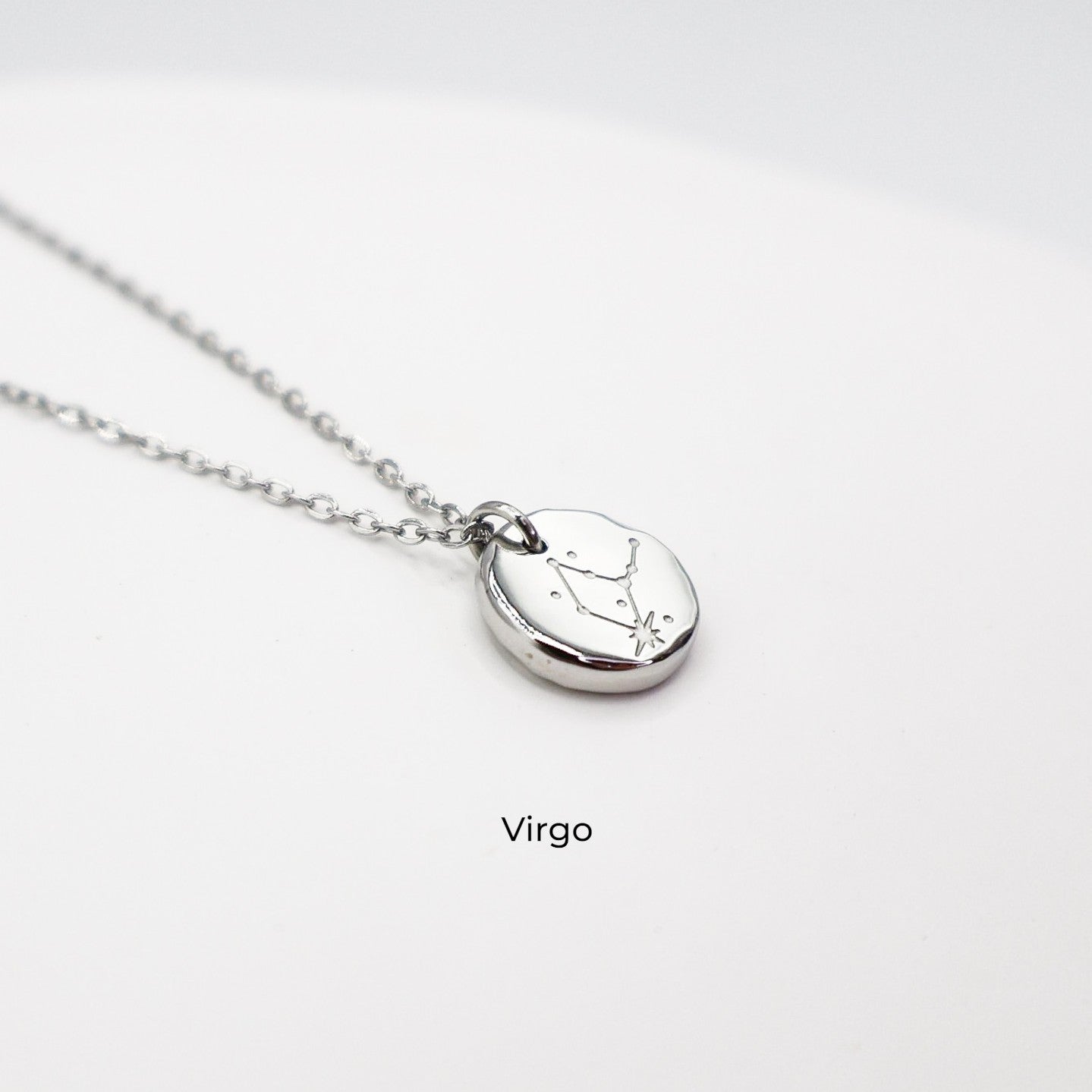 Silver necklace with a round pendant on a light gray background. The pendant is engraved with the Virgo star sign constellation